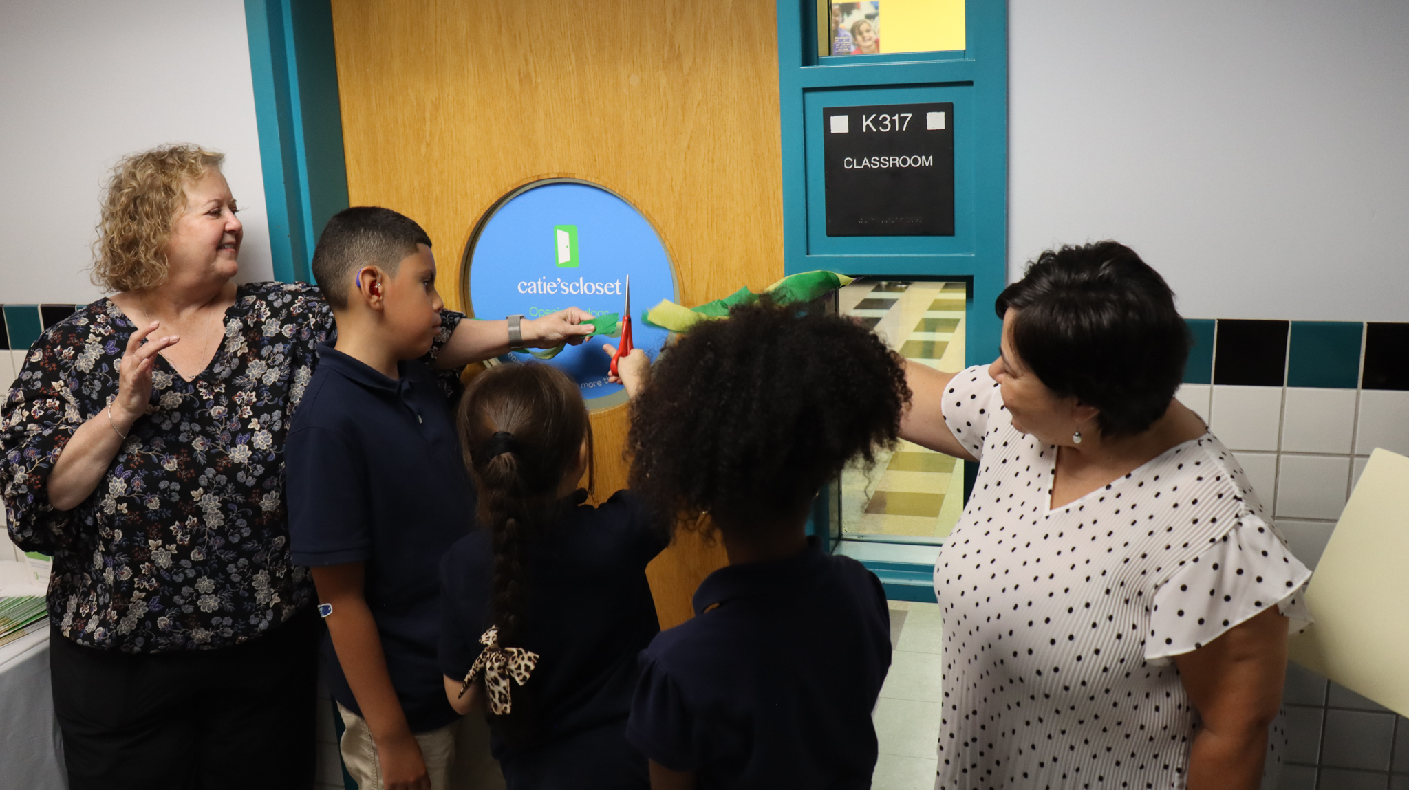 Students cutting a ceremonial ribbon in front of classroom door. 